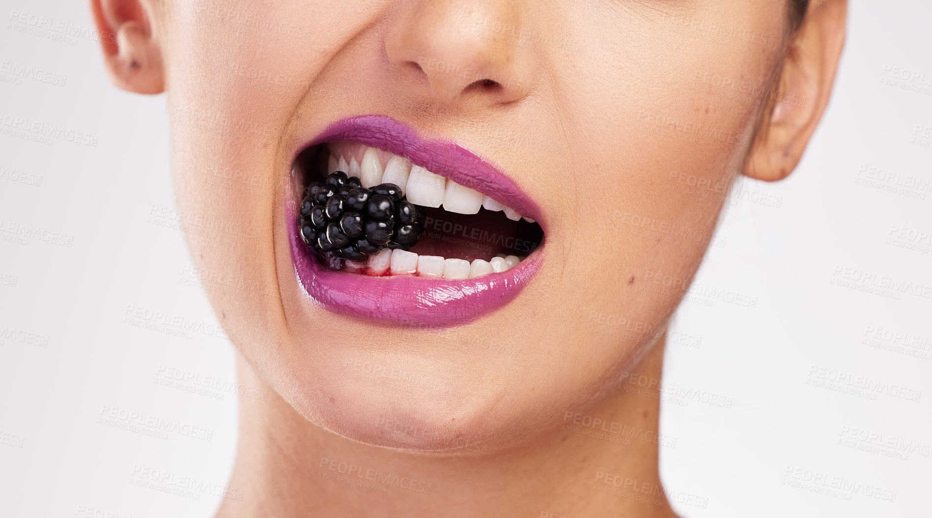 Buy stock photo Cropped shot of an attractive woman wearing purple lipstick and biting a blackberry against a studio background
