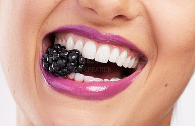 Buy stock photo Cropped shot of an attractive woman wearing purple lipstick and biting a blackberry against a studio background