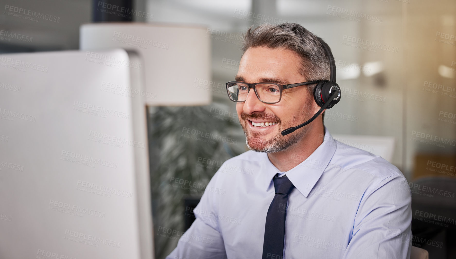 Buy stock photo Shot of a call centre agent wearing a headset while working on his computer