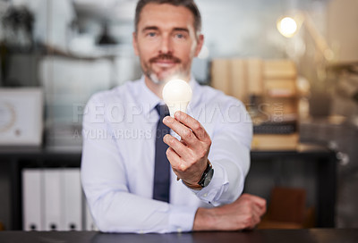 Buy stock photo Shot of a businessman holding a lightbulb while sitting at his desk