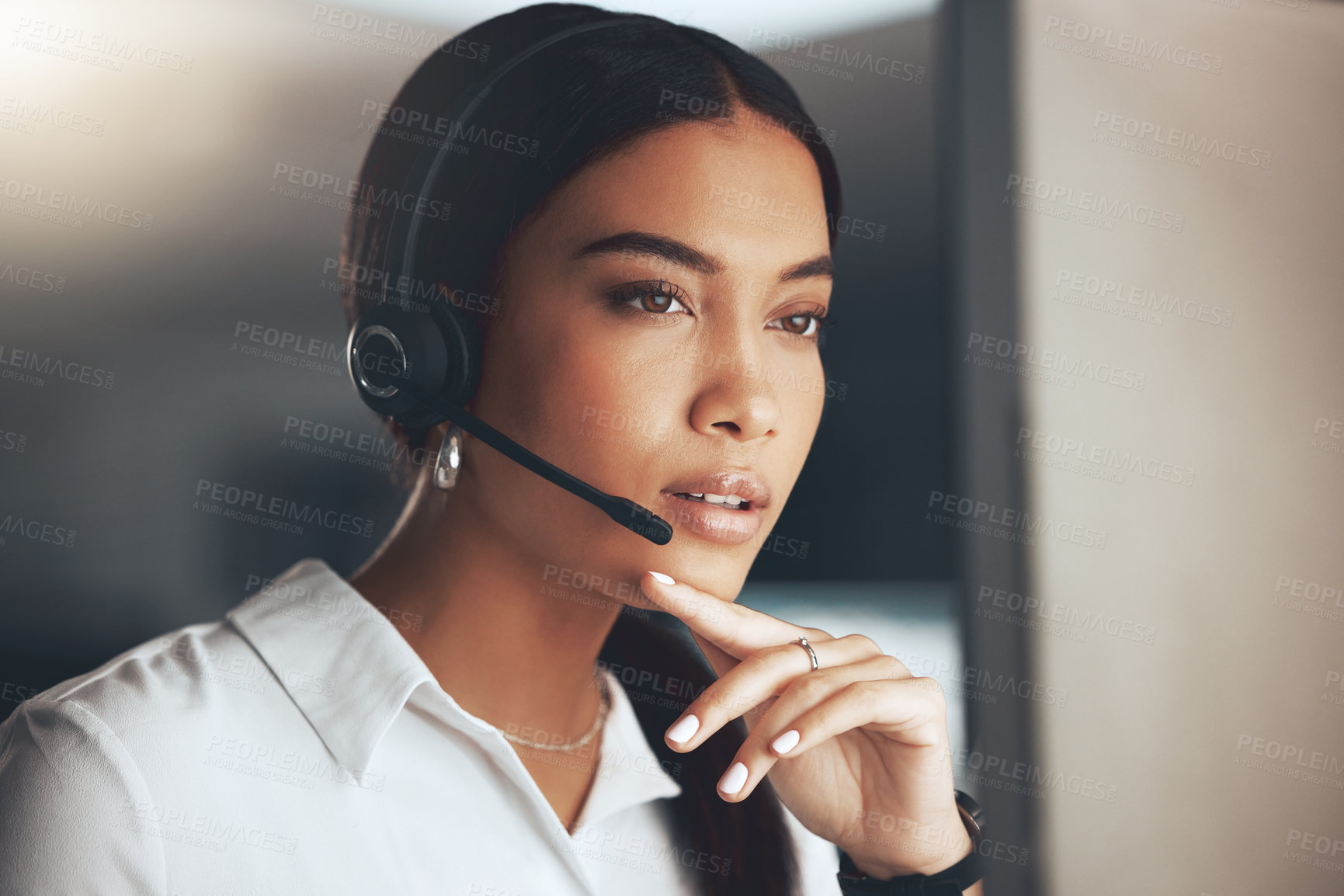 Buy stock photo Shot of a young call centre agent sitting alone in the office and looking contemplative while using her computer