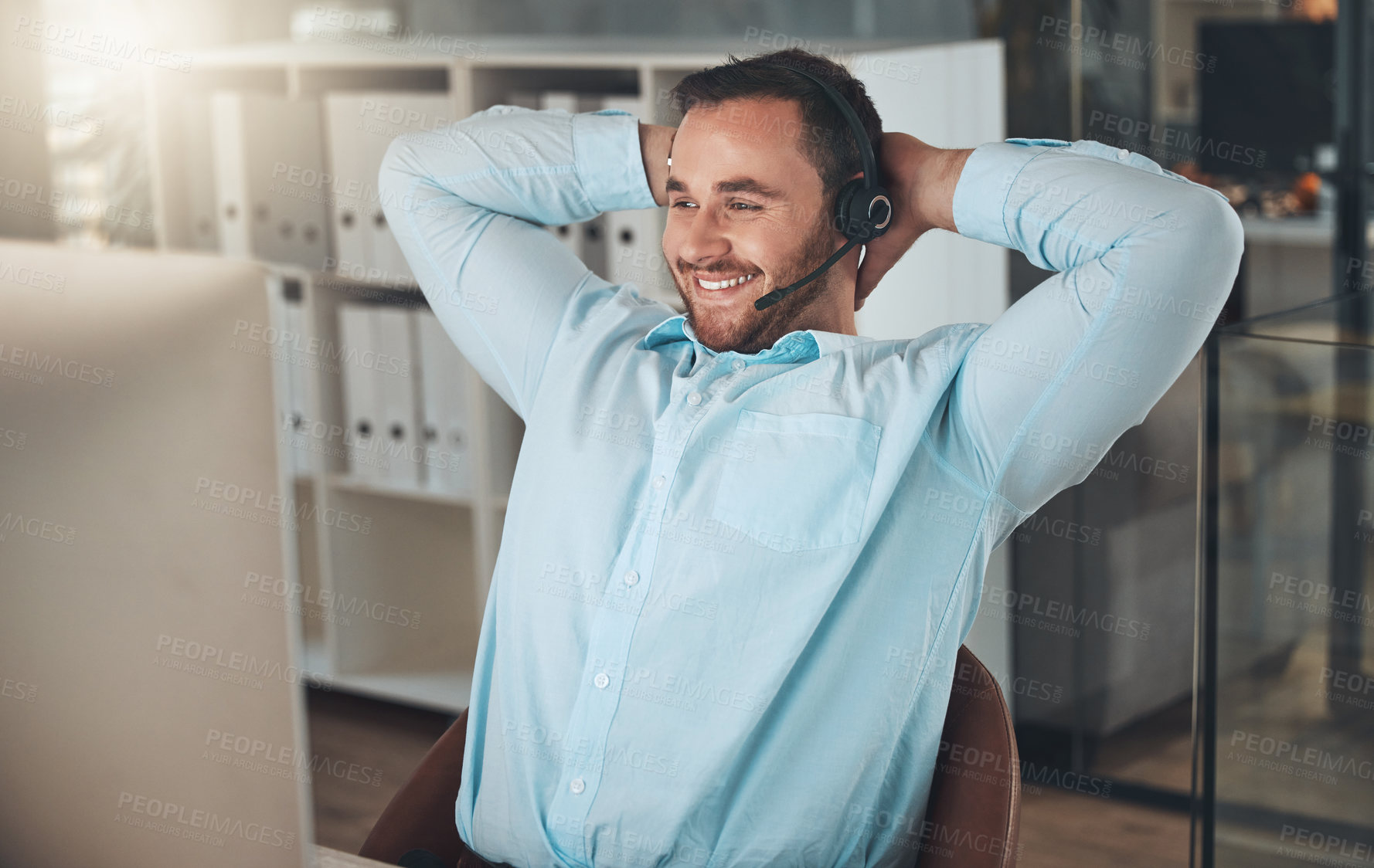 Buy stock photo Shot of a young call centre agent sitting in the office with his hands behind his head and feeling accomplished