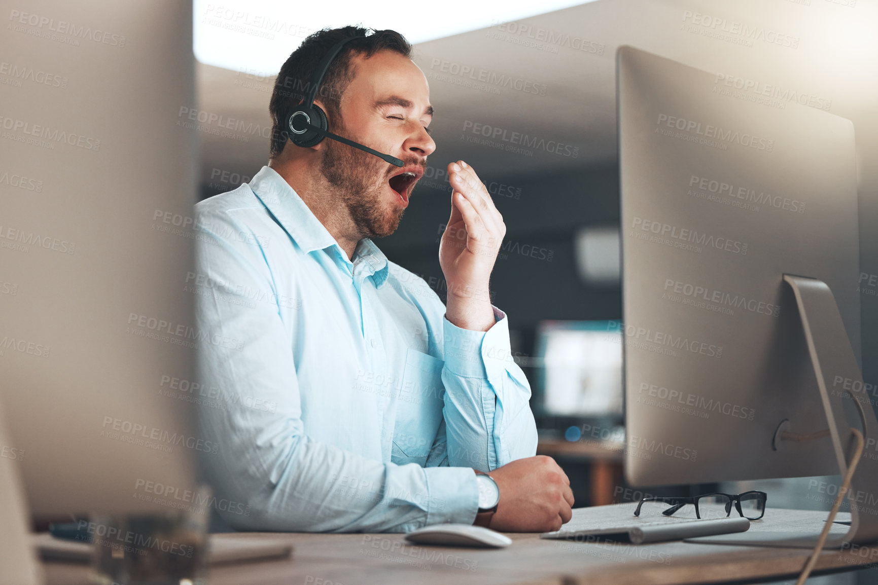 Buy stock photo Shot of a young call centre agent sitting alone in his office and yawning