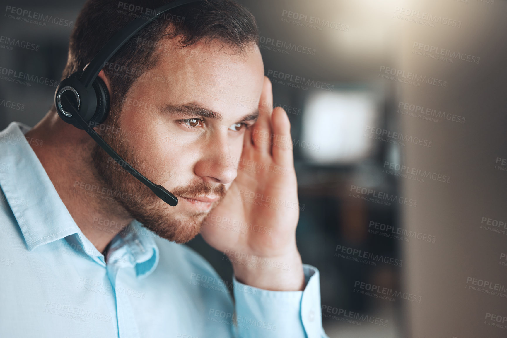 Buy stock photo Shot of a young call centre agent sitting alone in his office and looking contemplative while using his computer