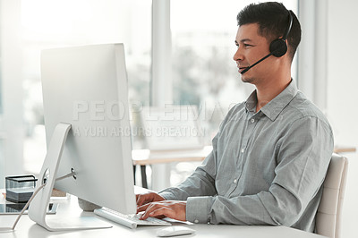 Buy stock photo Shot of a young male call center agent using a computer in an office at work