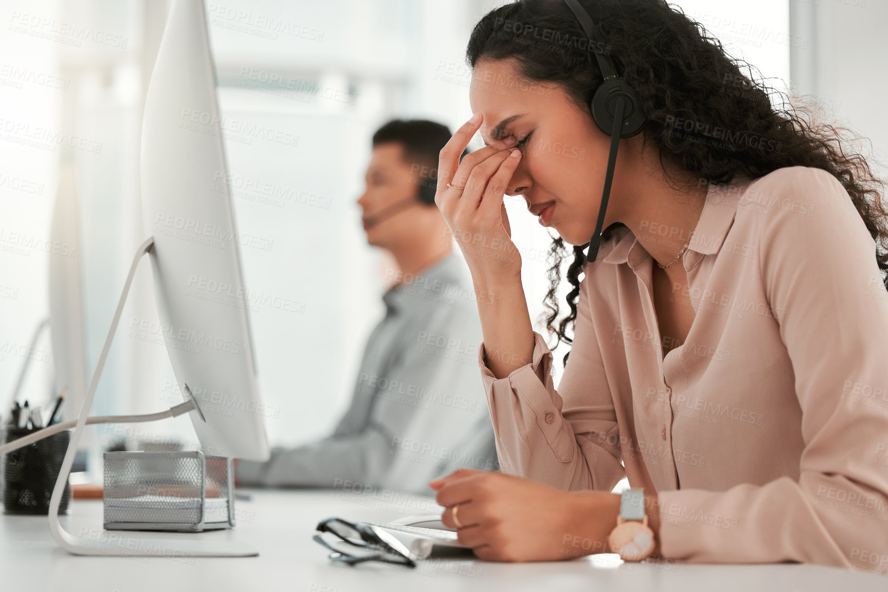 Buy stock photo Shot of a young female call center agent suffering from a headache in an office at work