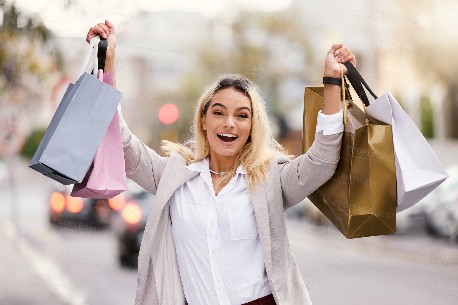 Buy stock photo Cropped portrait of an attractive young woman raising her bags after a successful day of shopping in the city