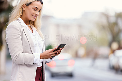 Buy stock photo Cropped shot of an attractive young businesswoman texting while walking through the city