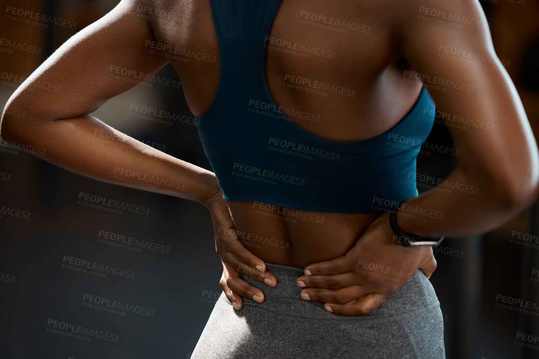 Buy stock photo Rearview shot of an unrecognizable and athletic young woman holding her lower back in pain while at the gym