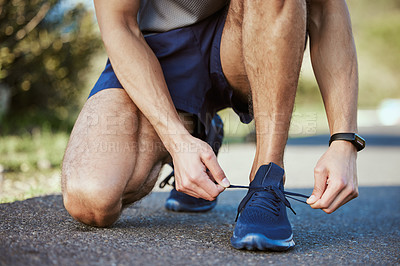 Buy stock photo Closeup shot of an unrecognisable man tying his shoelaces while exercising outdoors