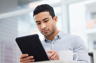 Buy stock photo Shot of a young businessman drinking coffee while using his digital tablet