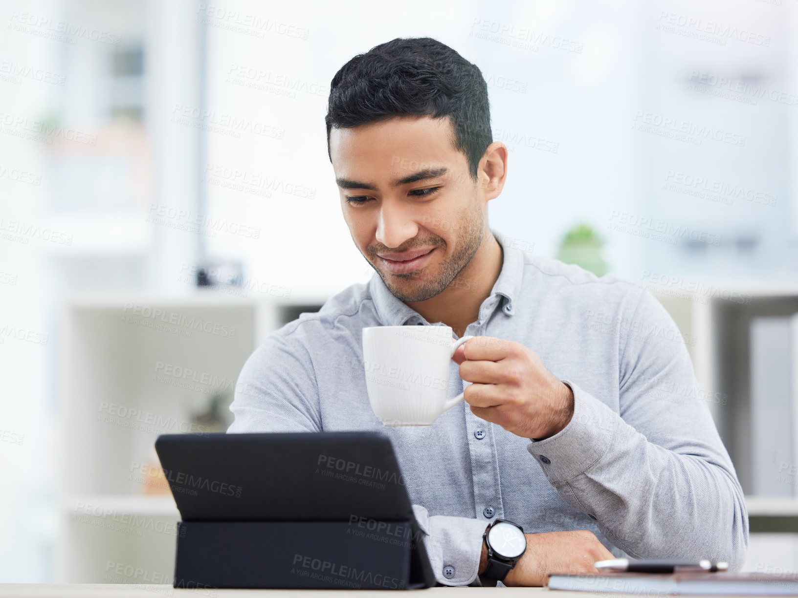 Buy stock photo Shot of a young businessman drinking coffee while using his digital tablet