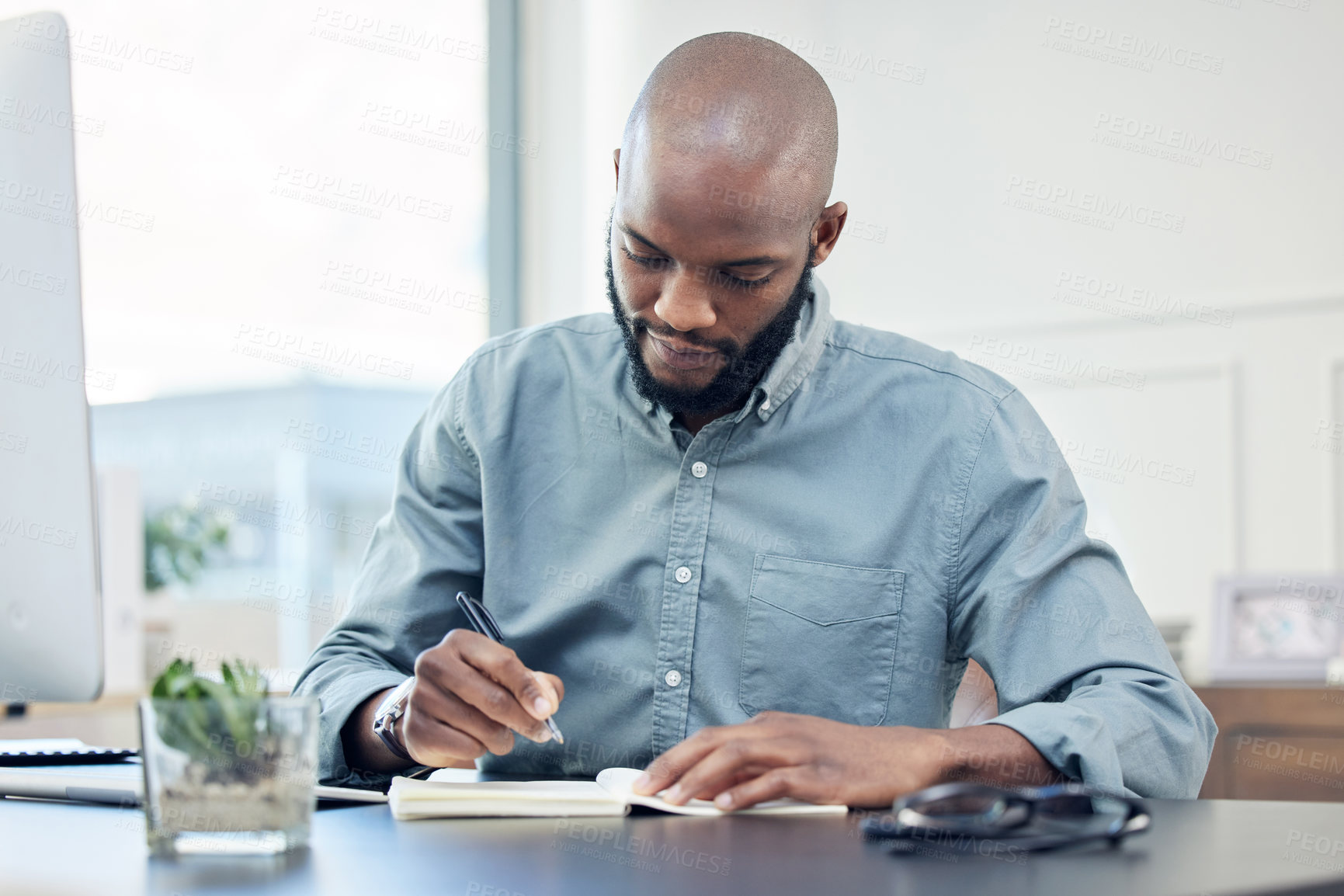 Buy stock photo Shot of a handsome young businessman sitting alone in the office and writing in his notebook