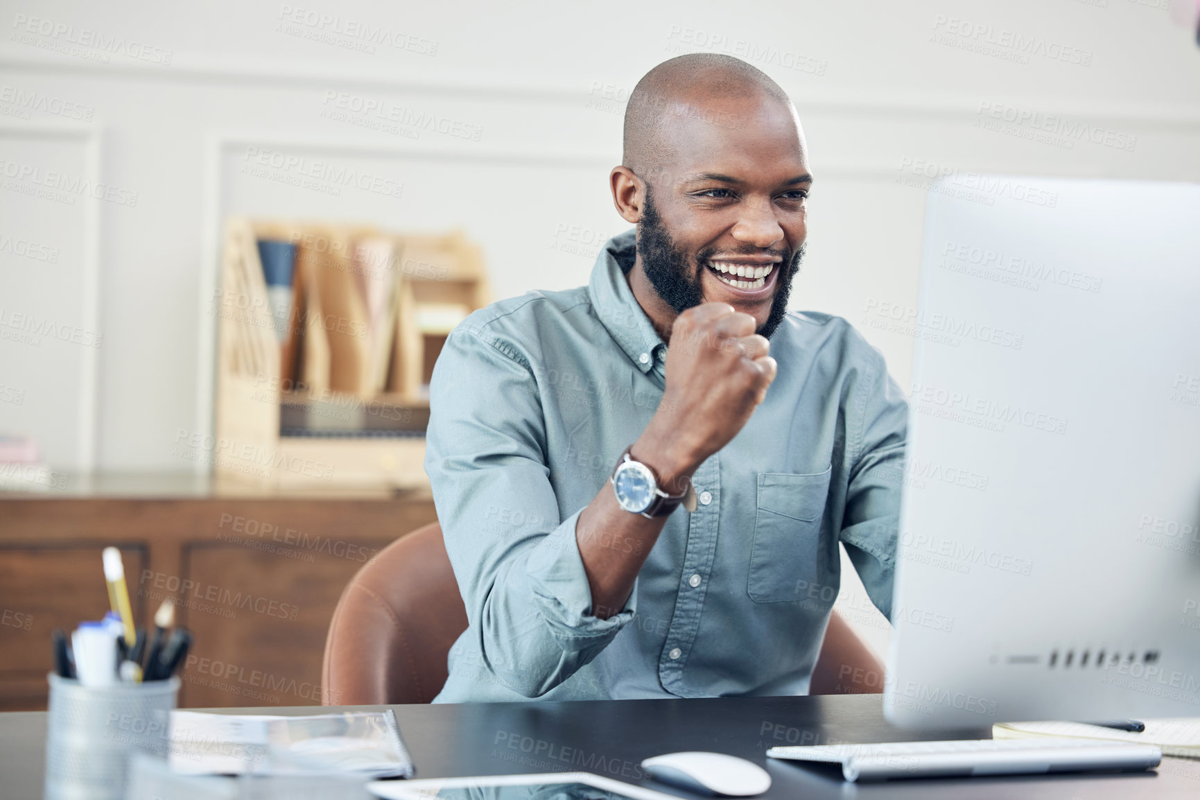 Buy stock photo Shot of a handsome young businessman sitting alone in his office and celebrating a success while using his computer