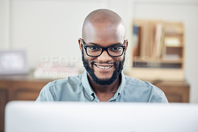 Buy stock photo Shot of a handsome young businessman sitting alone in his office and using his computer