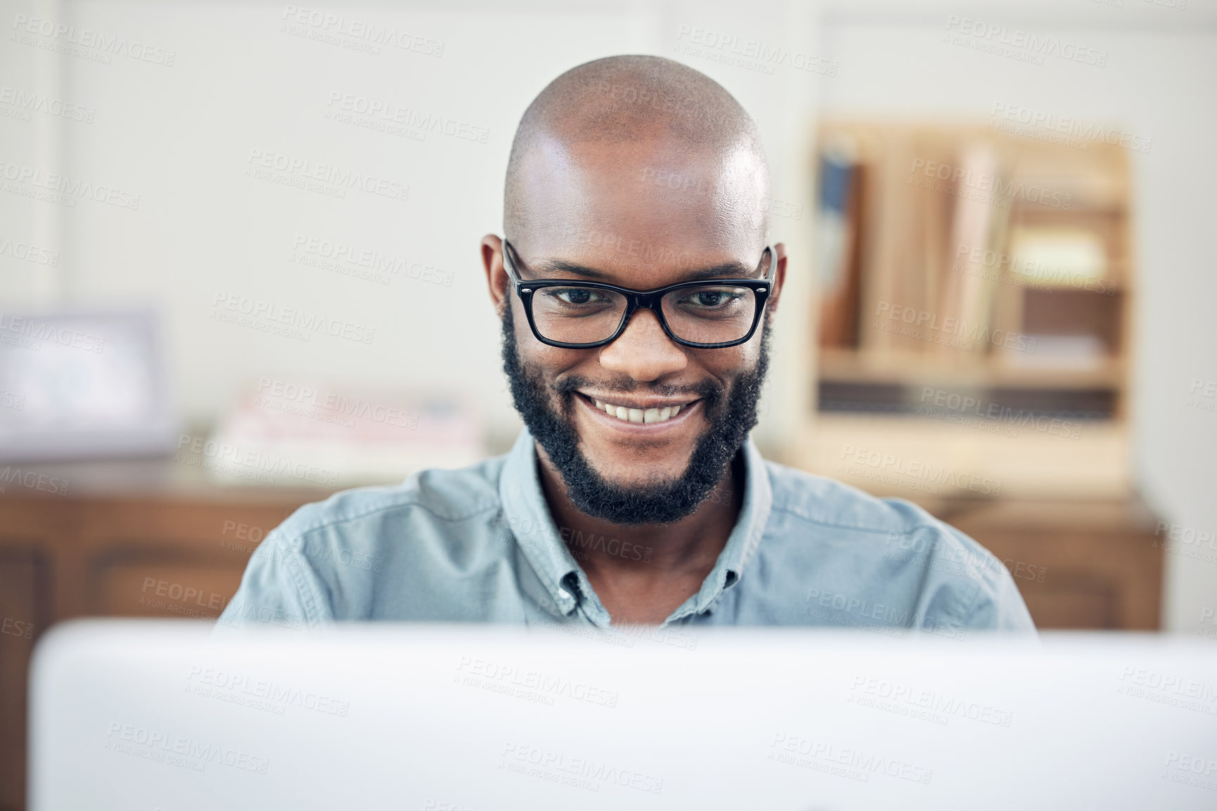 Buy stock photo Shot of a handsome young businessman sitting alone in his office and using his computer