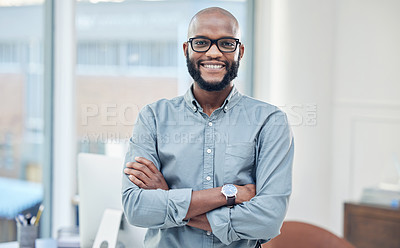 Buy stock photo Shot of a handsome young businessman standing alone in his office with his arms folded