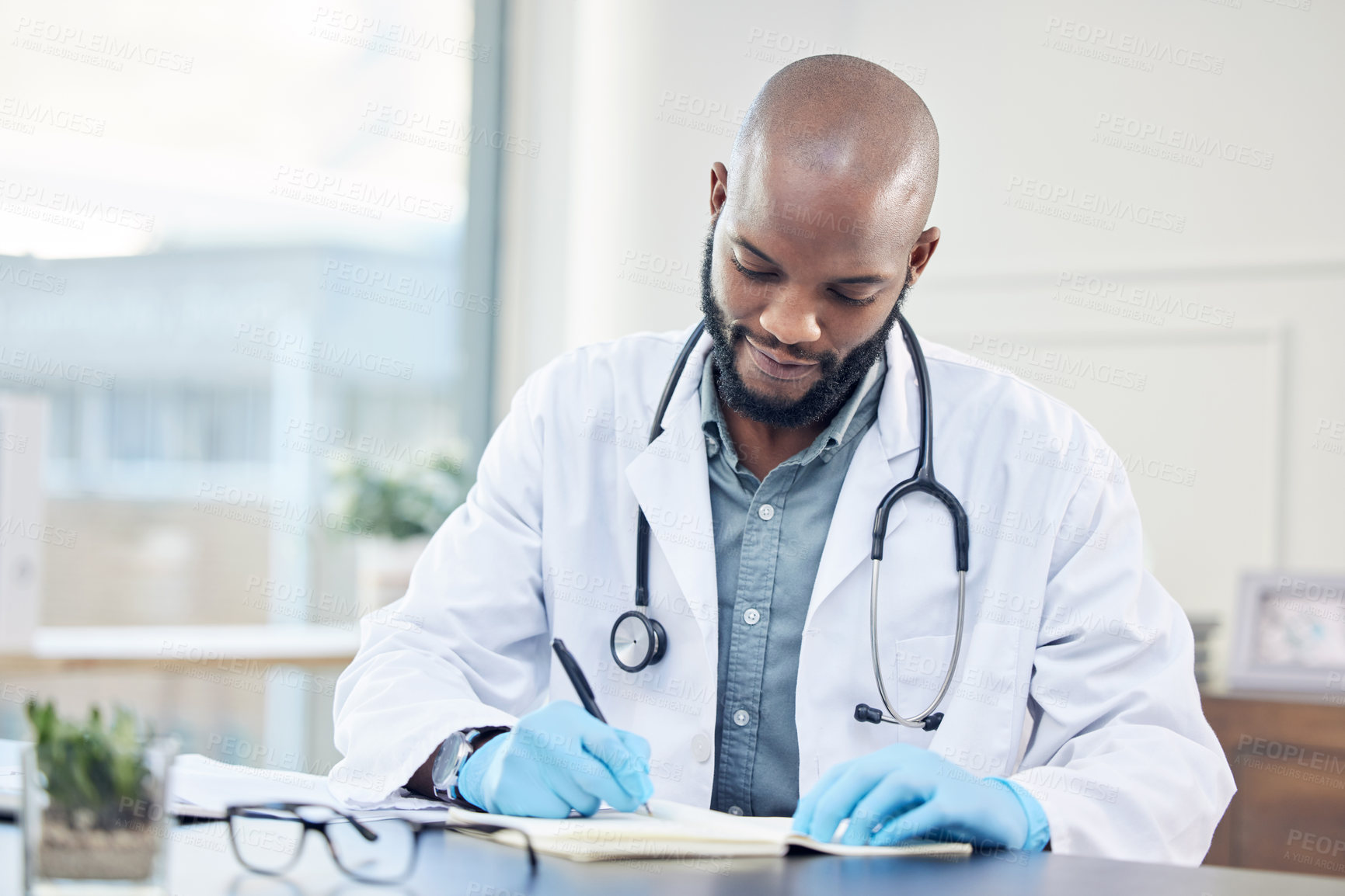 Buy stock photo Shot of a handsome young doctor sitting alone in his clinic and making notes