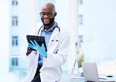Buy stock photo Shot of a handsome young doctor sitting alone in his clinic and using a digital tablet