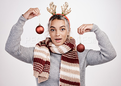 Buy stock photo Studio portrait of an attractive young woman holding up baubles while dressed in Christmas-themed attire