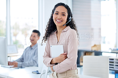 Buy stock photo Shot of a young call centre agent sitting and holding a digital table while her colleague works behind her
