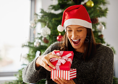 Buy stock photo Shot of a young woman opening presents during Christmas at home