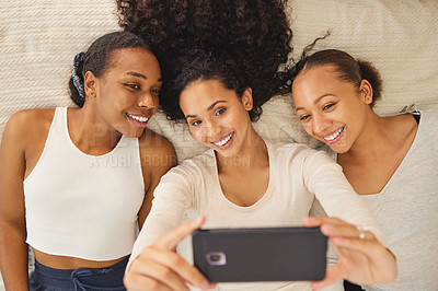 Buy stock photo Shot of three girlfriends taking a selfie while lying on a bed together