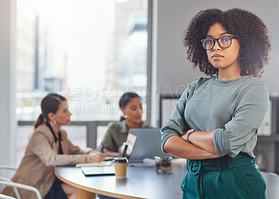 Buy stock photo Portrait of a young businesswoman folding her arms while her colleagues have a meeting in the background