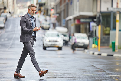 Buy stock photo Shot of a handsome businessman walking through the city while using his smartphone