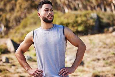 Buy stock photo Shot of a handsome young man standing alone outside with his hands on his hips after a run