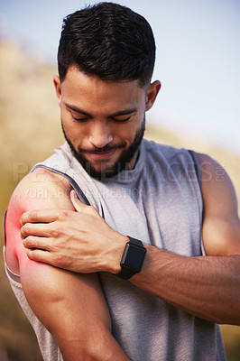 Buy stock photo Shot of a handsome young man standing alone outside and suffering from a sore shoulder during his run