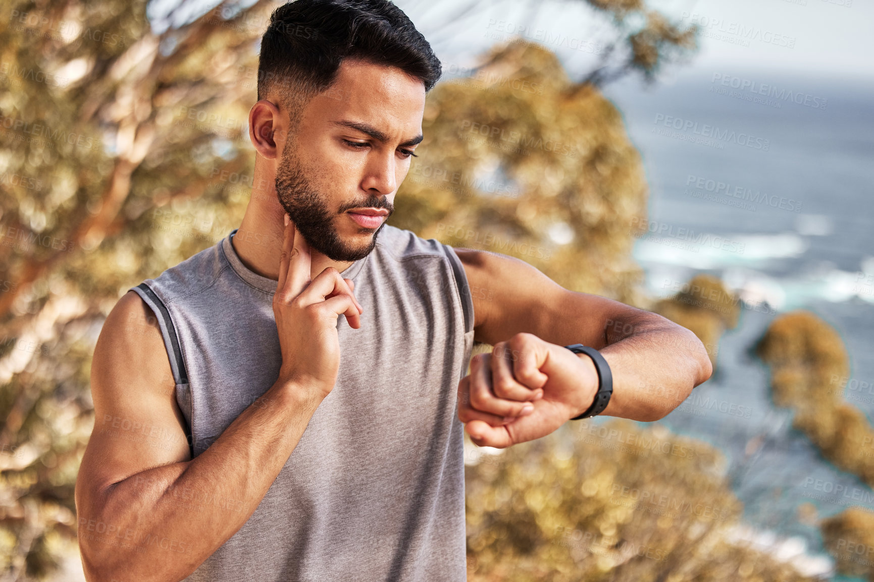 Buy stock photo Shot of a handsome young man standing alone outside and using his watch to time his pulse after a run