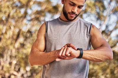 Buy stock photo Shot of a handsome young man standing alone and setting a timer on his watch before running outside