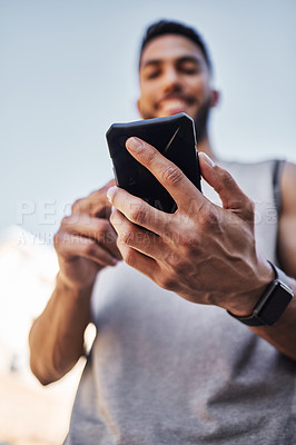 Buy stock photo Shot of a young man standing alone outside and using his cellphone during his run