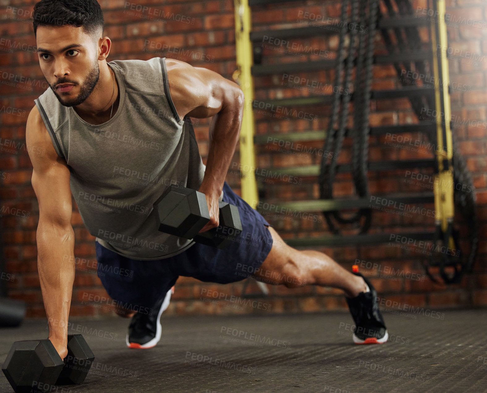 Buy stock photo Shot of a young man working out with dumbbells in a gym