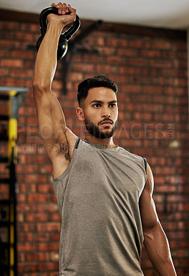 Buy stock photo Shot of a young man working out with a kettle bell in a gym