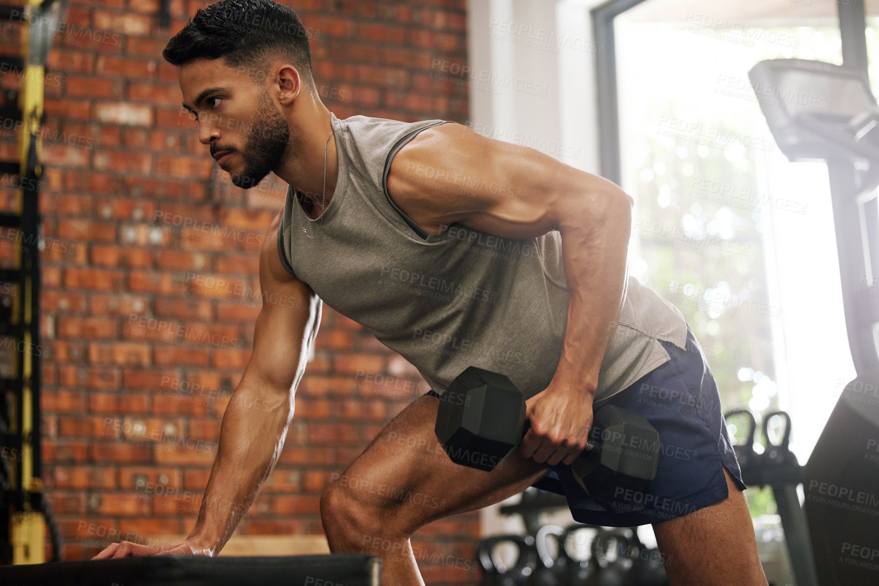 Buy stock photo Shot of a young man working out with dumbbells in a gym