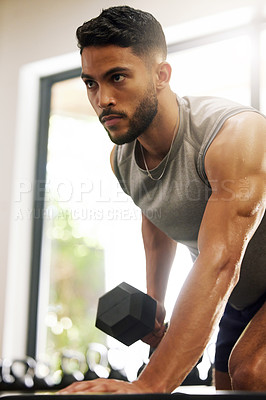 Buy stock photo Shot of a young man working out with dumbbells in a gym
