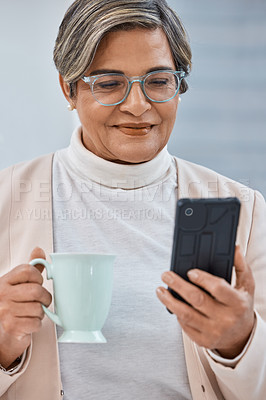 Buy stock photo Shot of a mature businesswoman drinking coffee while using a cellphone in an office
