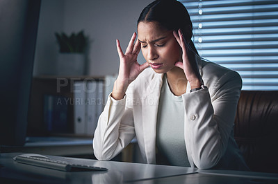 Buy stock photo Shot of an attractive young businesswoman sitting alone in the office at night and suffering from a headache