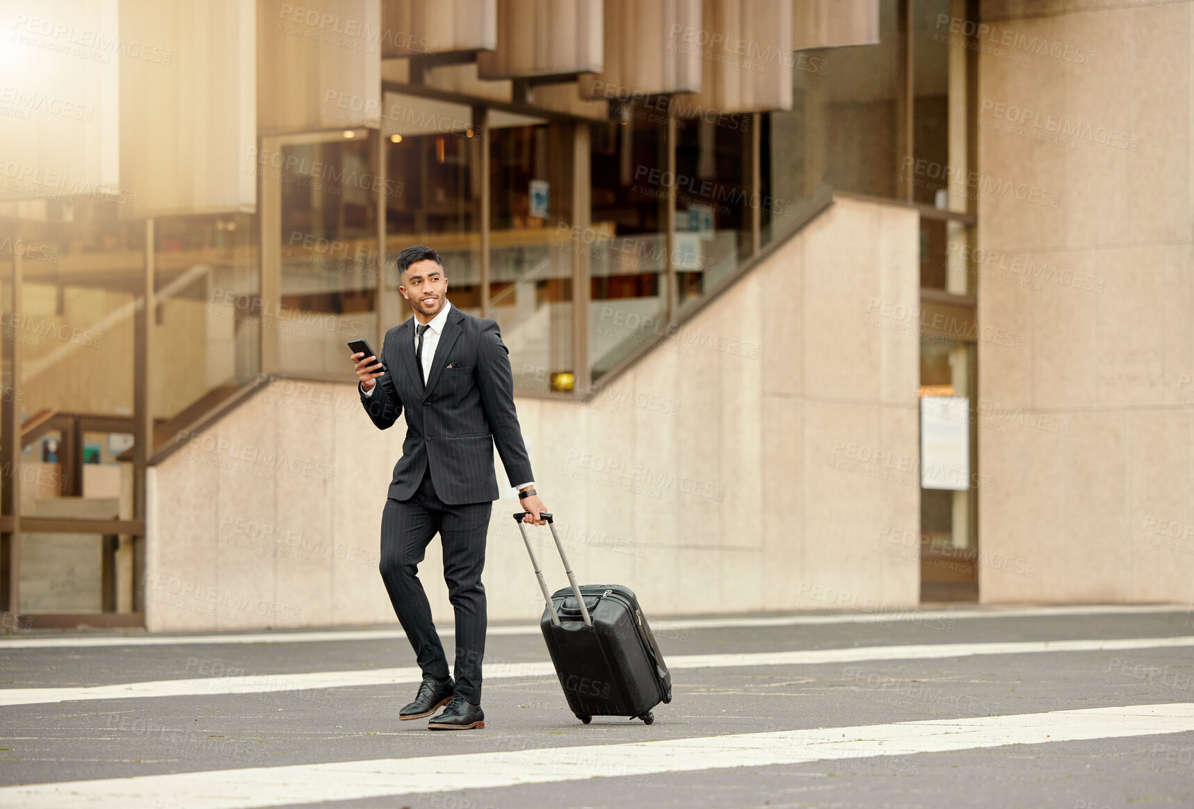 Buy stock photo Shot of a businessman walking around town with his luggage using his smartphone