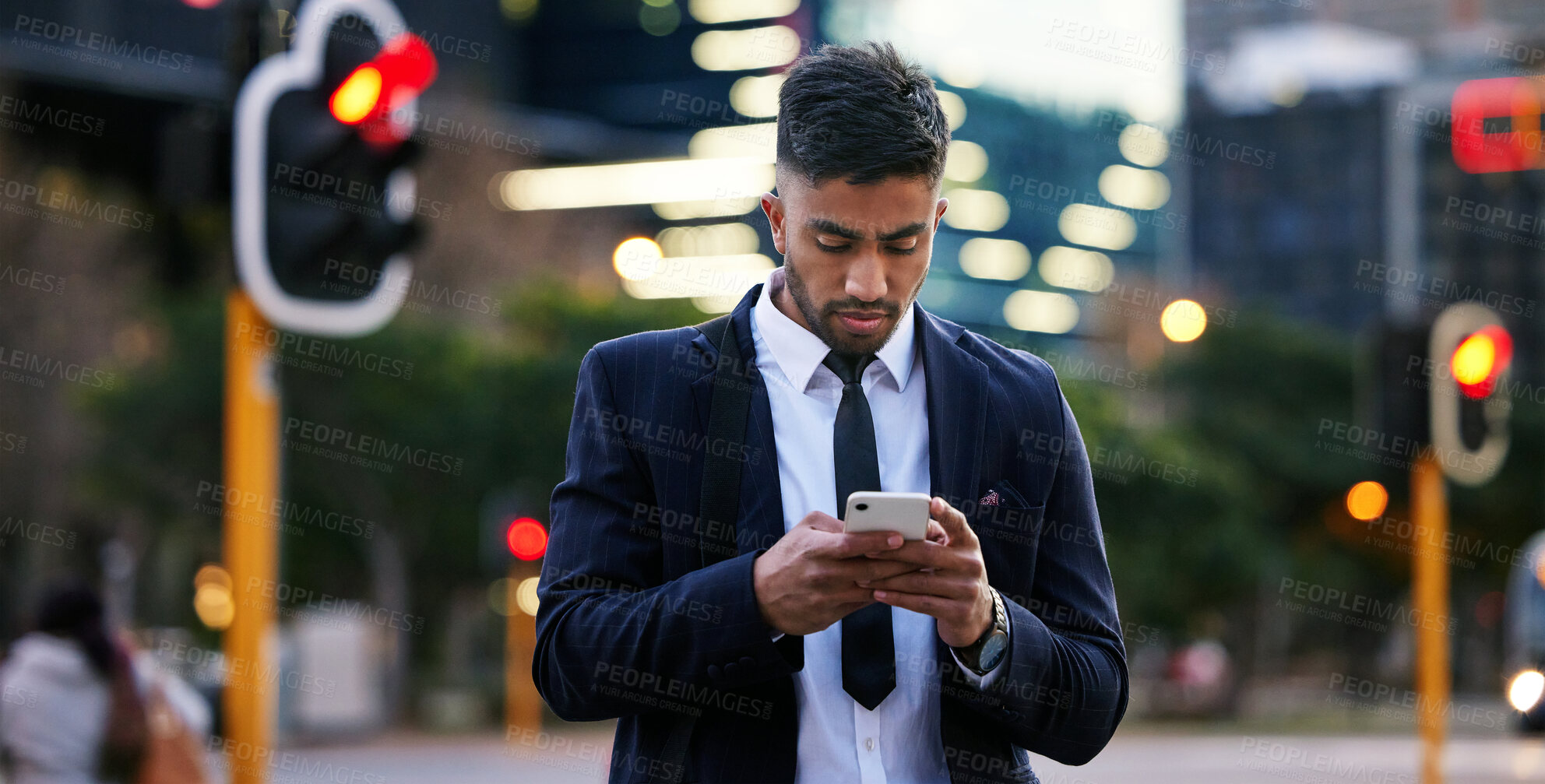 Buy stock photo Shot of a handsome young businessman walking around town using his smartphone