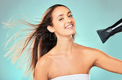 Buy stock photo Studio portrait of an attractive young woman blowdrying her hair against a blue background