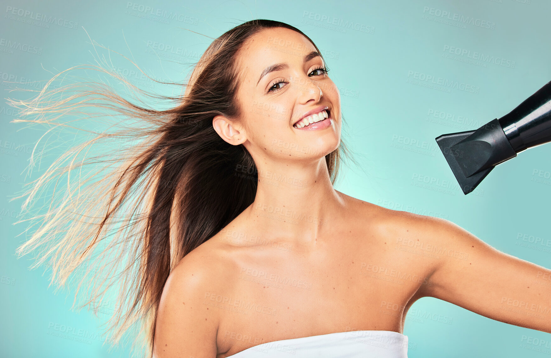 Buy stock photo Studio portrait of an attractive young woman blowdrying her hair against a blue background