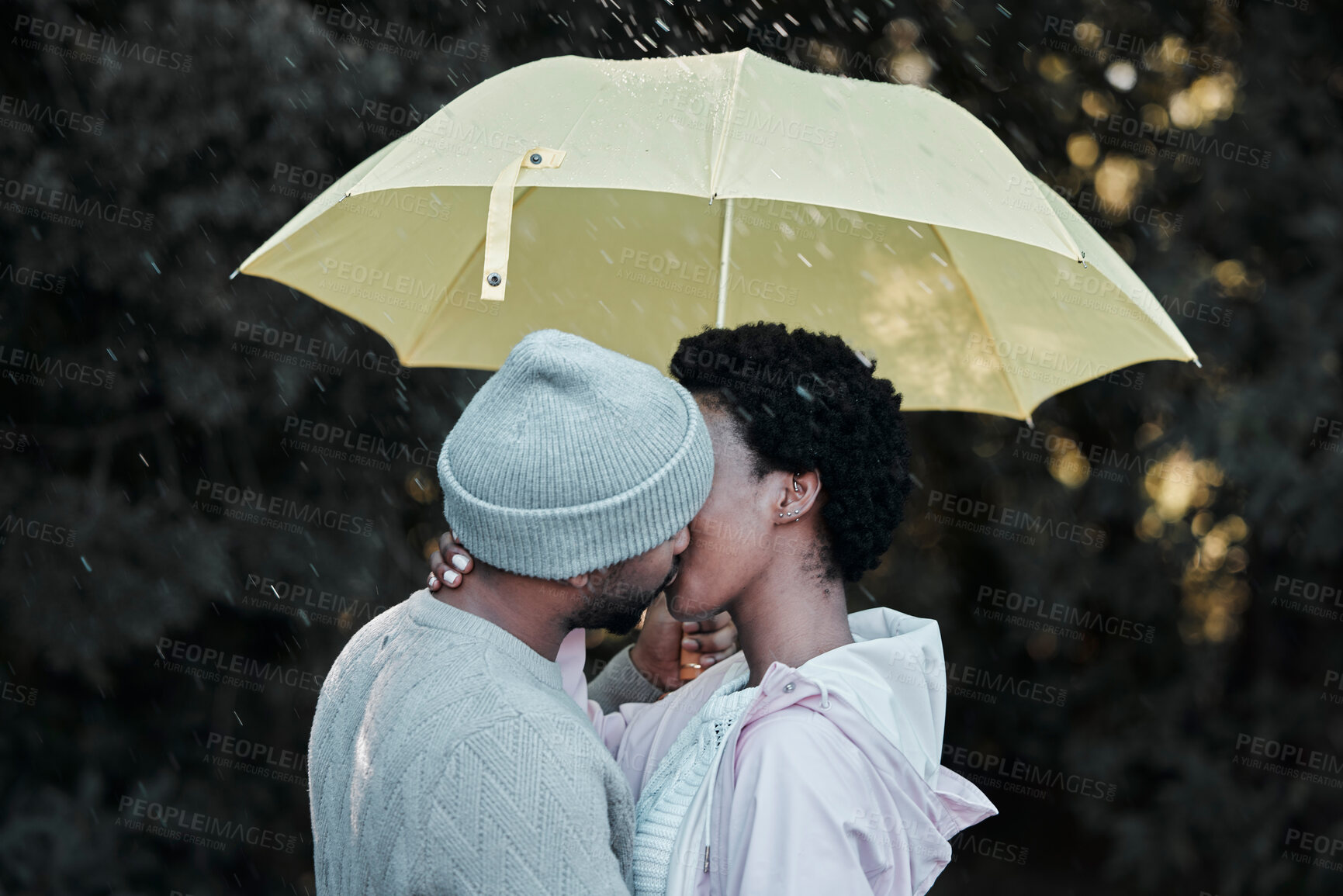 Buy stock photo Shot of a young couple kissing while standing under an umbrella