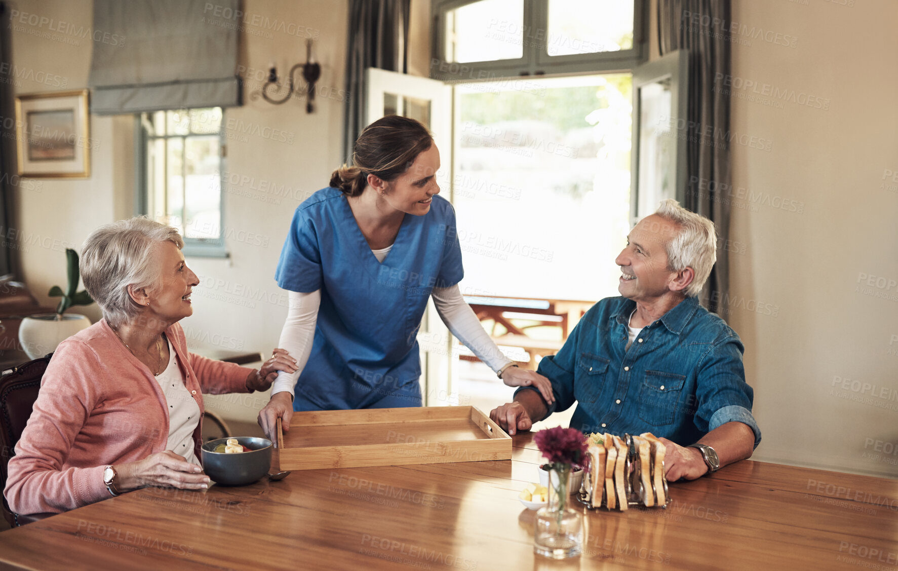 Buy stock photo Shot of a young nurse checking up on a senior couple during breakfast at a nursing home