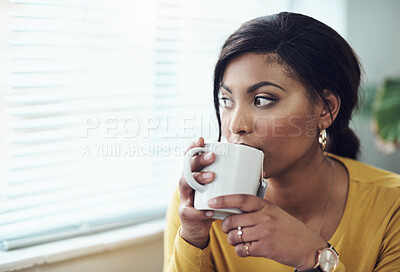 Buy stock photo Shot of an attractive young woman sitting alone at home and looking contemplative while drinking a cup of coffee