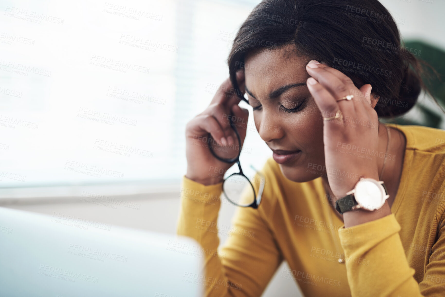 Buy stock photo Shot of an attractive young woman sitting alone at home and suffering from a headache while using her laptop