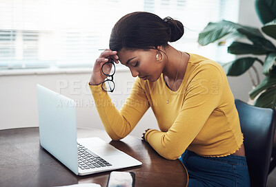 Buy stock photo Shot of an attractive young woman sitting alone at home and suffering from a headache while using her laptop