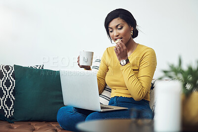 Buy stock photo Shot of an attractive young woman sitting alone at home and eating while using her laptop